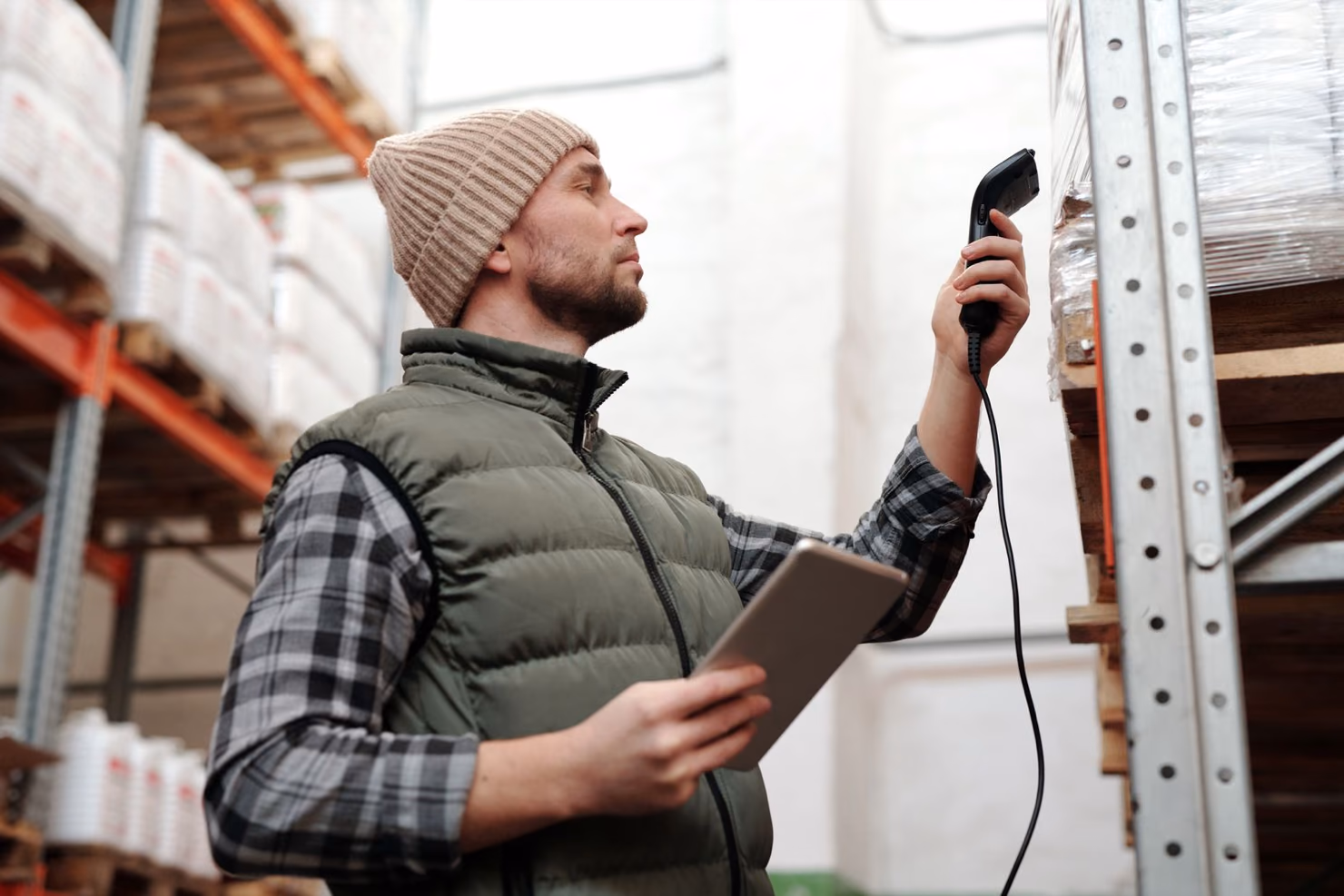 A warehouse worker scanning stock on a pallet with a handheld barcode scanner while holding a tablet.
